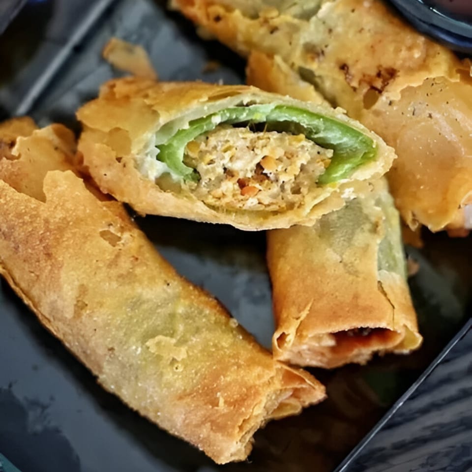 Close-up of golden-fried Filipino lumpia, one cut open revealing green pepper and savory filling.