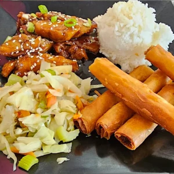 Filipino meal with chicken adobo, rice, lumpia, and a side of coleslaw on a black plate.