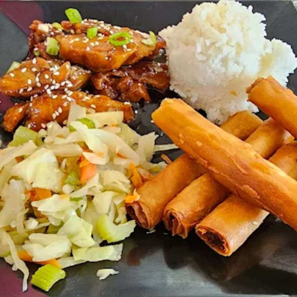 Filipino meal with chicken adobo, rice, lumpia, and a side of coleslaw on a black plate.