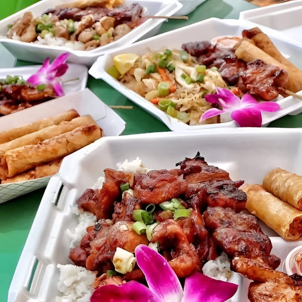 Multiple Kain Na-Filipino Cuisine takeout containers filled with various Filipino dishes, including lumpia and skewers.