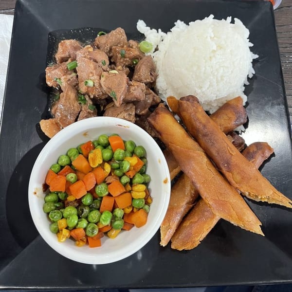 Filipino meal with meat, rice, spring rolls, and a side of peas and carrots on a black plate.